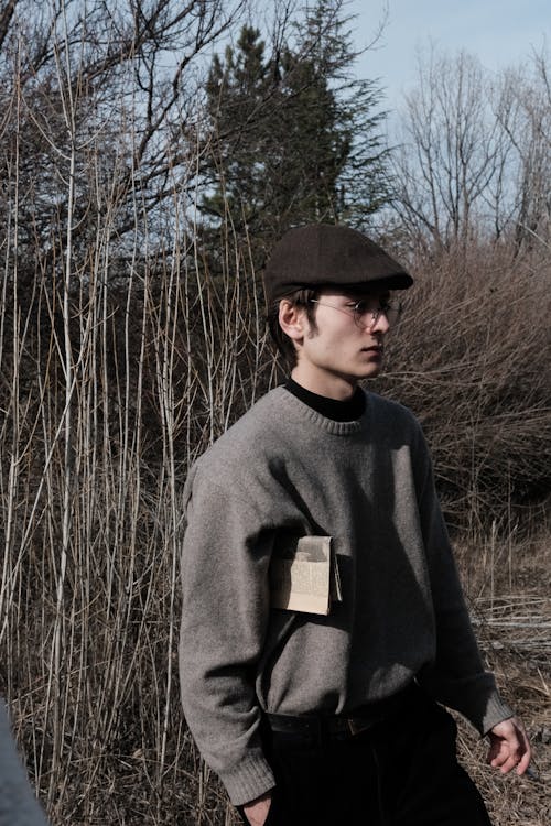 A Young Man in a Sweater, Cap and Eyeglasses Standing Outside 