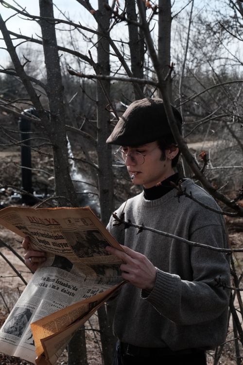 Free A man in vintage attire reads a newspaper in a park, surrounded by bare trees. Stock Photo