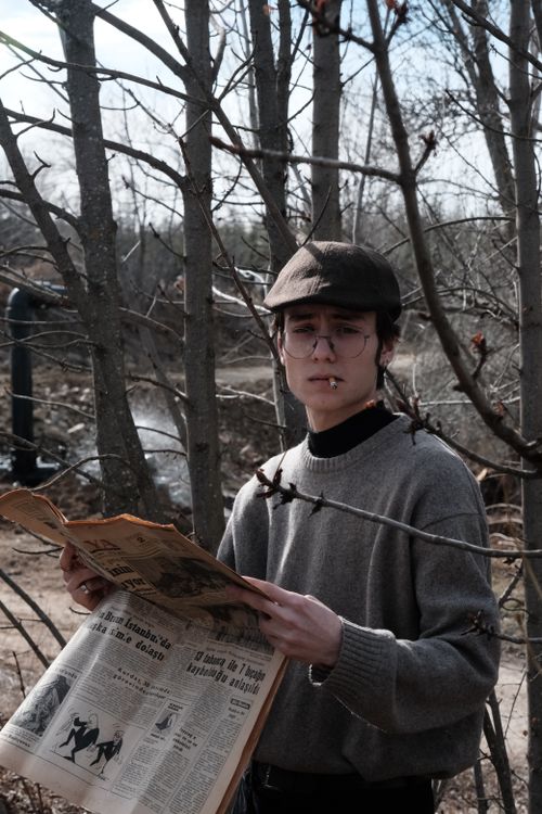 Free A young man with eyeglasses and a cap reads a newspaper in a fall park. Stock Photo