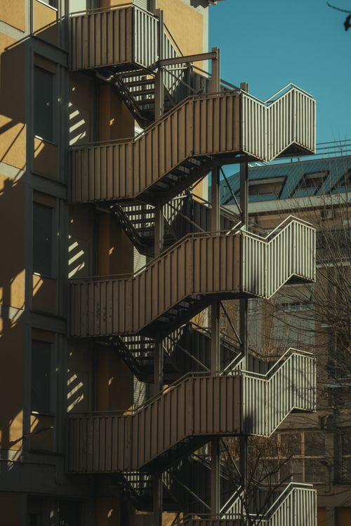 Free Exterior view of a building showcasing metal staircases and shadows on a sunny day. Stock Photo