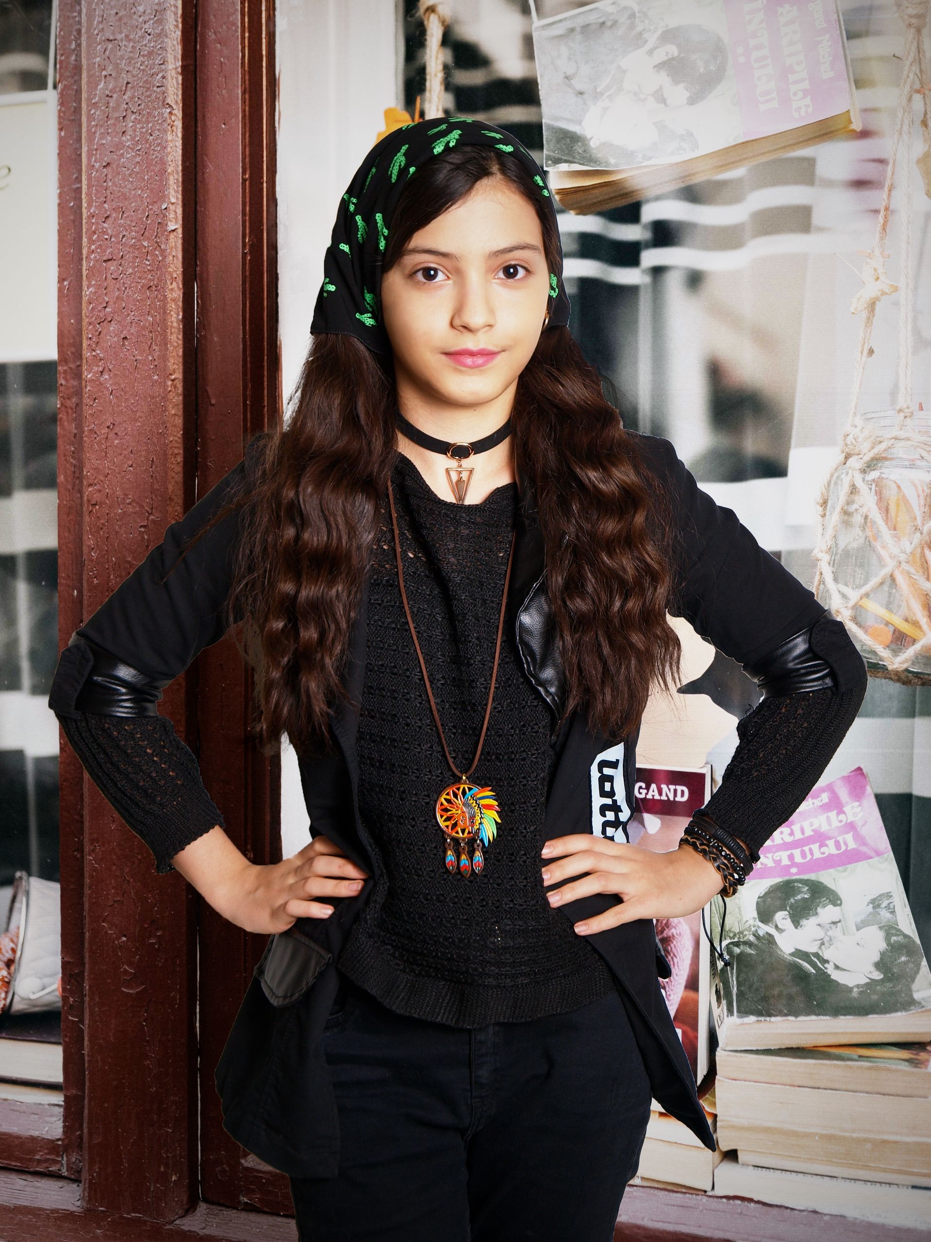 Confident young woman in black with headscarf and dreamcatcher necklace near bookstore window.