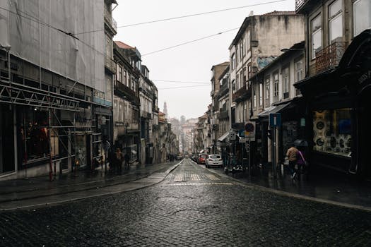 Gloomy urban street scene on a rainy day in Porto, Portugal, with cobblestone pavement and pedestrians.