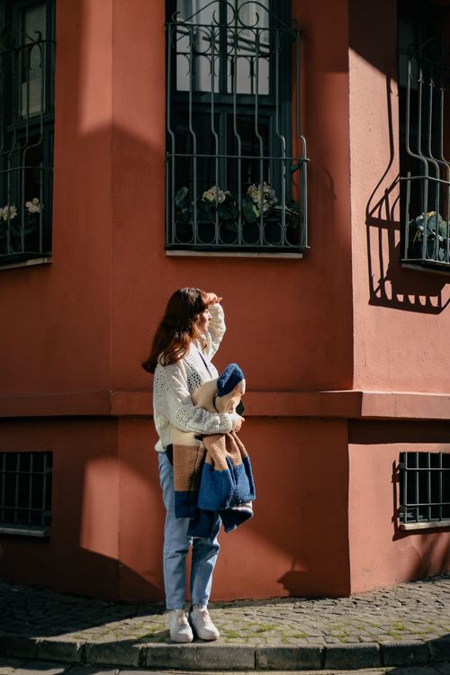 Free A woman stands on a sunlit urban corner, shielding her eyes from the sun. Stock Photo