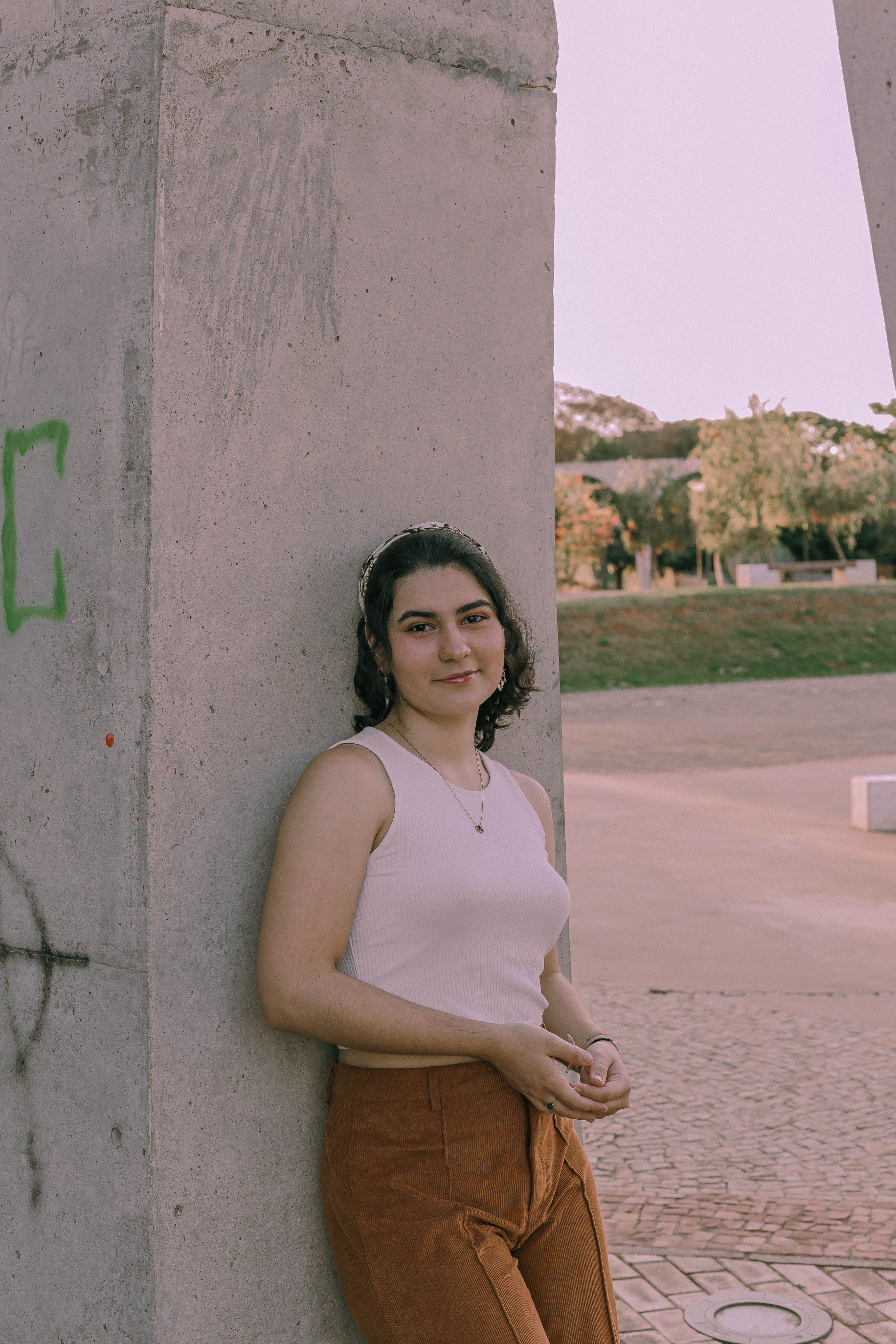 Young woman in fashionable attire leaning against a concrete structure in Brazil.