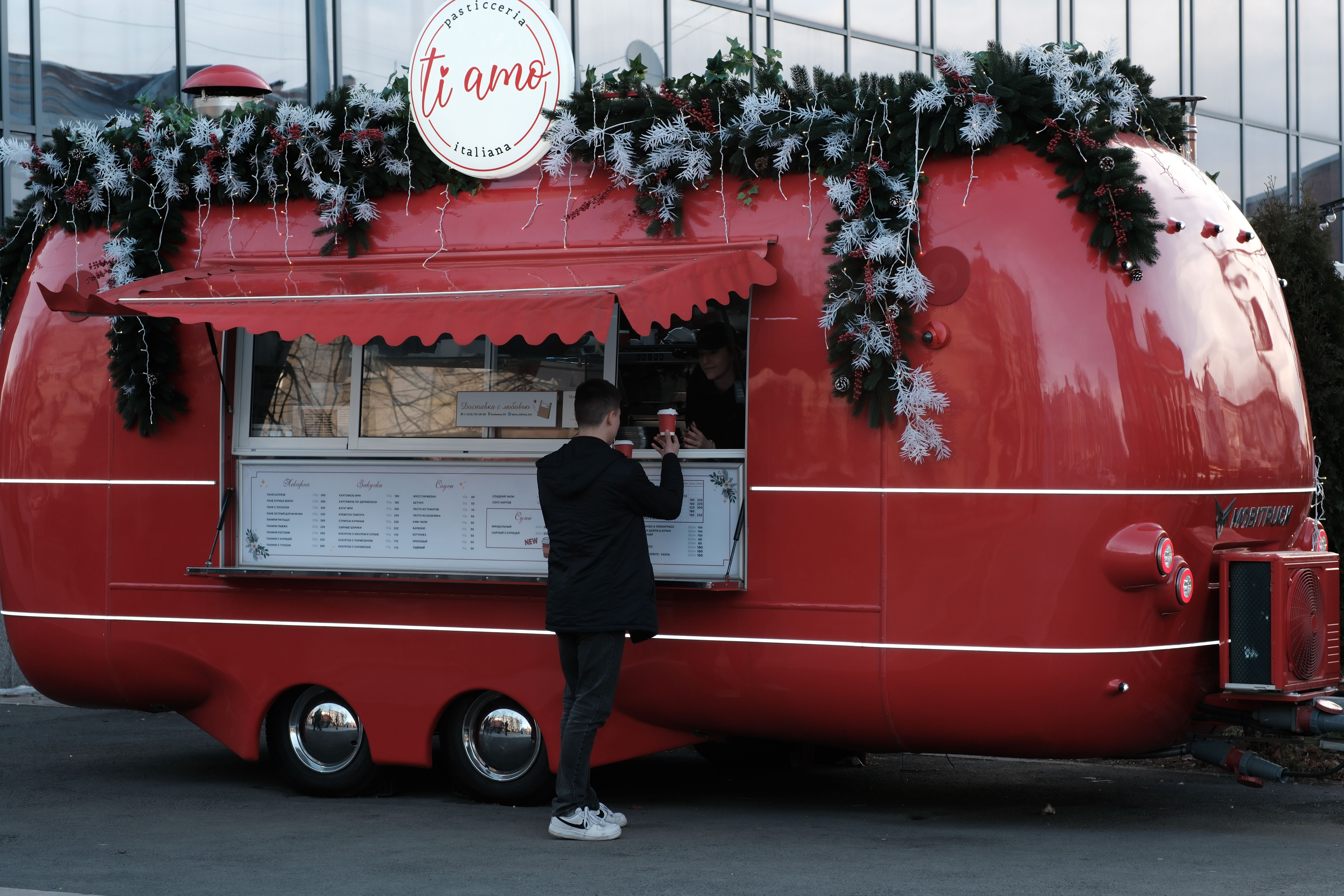 A vibrant red food truck adorned with festive Christmas decorations serving a customer.