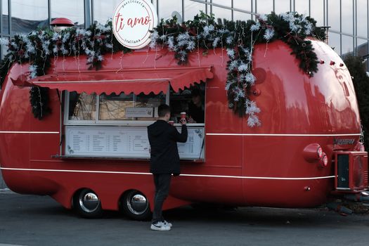 A vibrant red food truck adorned with festive Christmas decorations serving a customer.