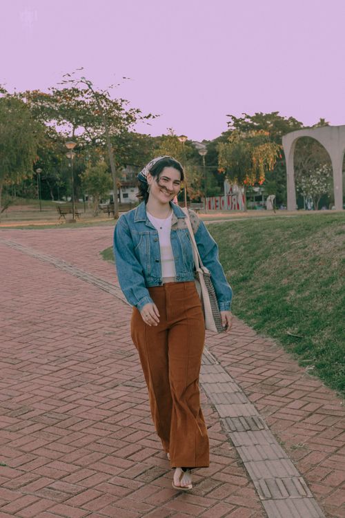 Free A smiling woman in a denim jacket strolls peacefully through a park at sunset. Stock Photo