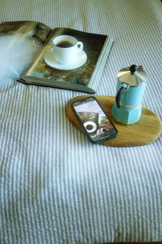 A warm and cozy setup of an open book, coffee cup, and moka pot on a striped cloth.