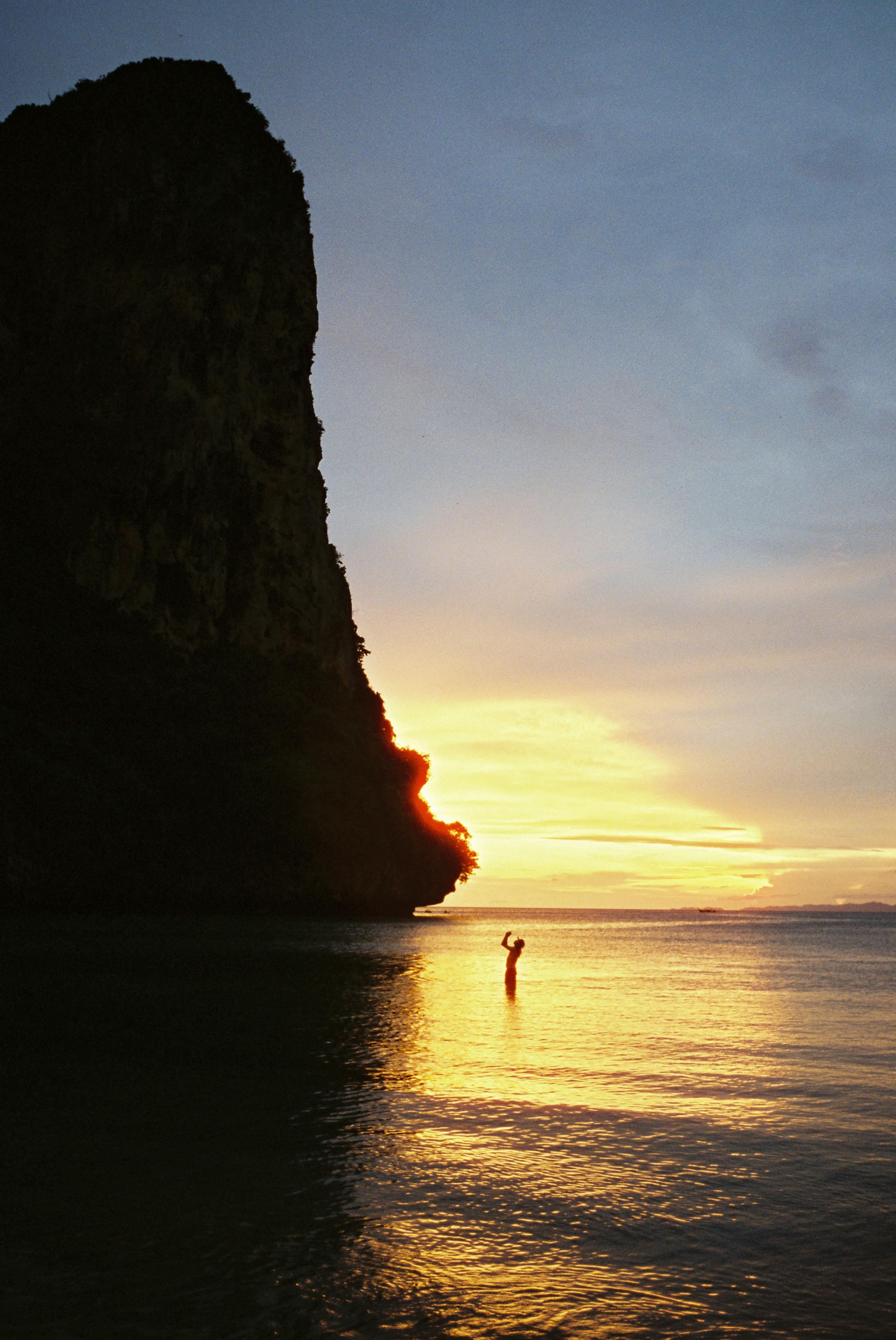 Dramatic silhouette of a cliff and person at Ao Nang Beach during sunset.