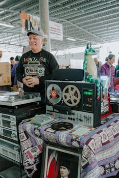 A man stands at a vintage market stall with retro audio equipment and decorations.