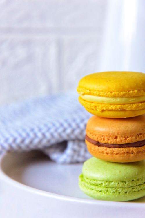 Free Close-up of colorful French macarons stacked on a white plate, perfect for dessert portrayals. Stock Photo