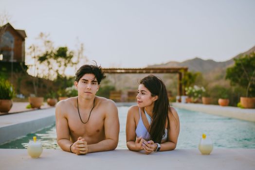 A couple enjoying a relaxing day by the pool in a summer resort setting, surrounded by nature.