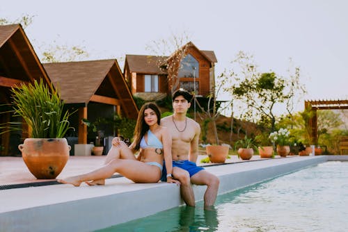 Free A couple sitting on the edge of a pool with a house in the background Stock Photo