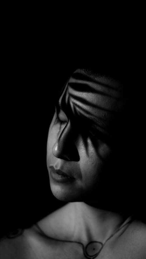 Black and White Photo of a Palm Leaf Casting Shadow on the Face of a Person 