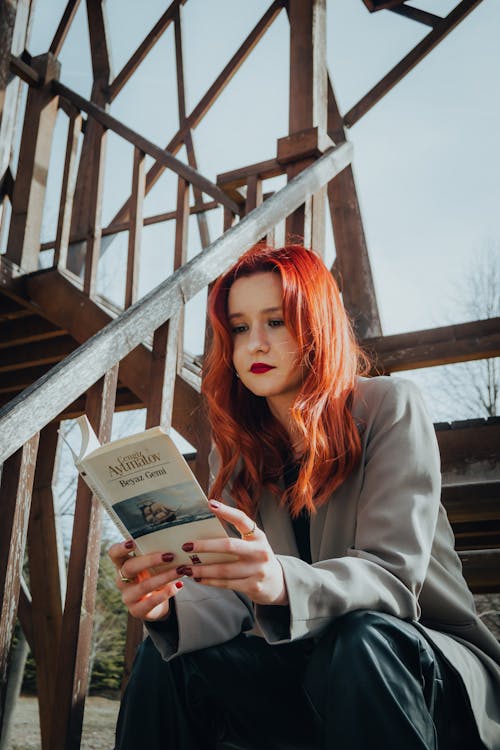 Beautiful Red Haired Woman Reading Book While Sitting on Stairs