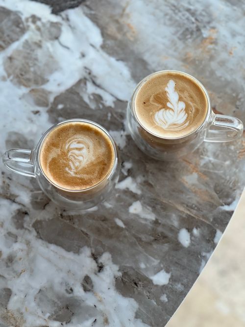 Free Close-up of two cappuccino cups with artful latte designs on a marble table, creating a cozy cafe atmosphere. Stock Photo