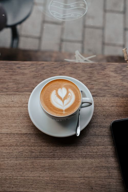 Free A beautifully crafted cappuccino with latte art on a wooden table in a cozy café setting. Stock Photo