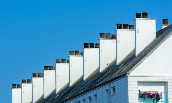 Chimney Cleaning โ Row of chimneys on modern residential buildings under a clear blue sky. Urban architecture with rooftops.