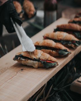 A close-up of delicious croissant sandwiches with greens being arranged by hand on a wooden board.