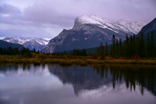 Captivating view of Banff's mountains reflected in a tranquil lake surrounded by autumn foliage.
