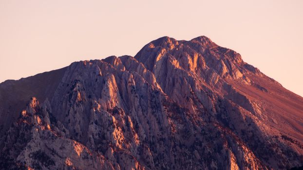 Majestic mountain peak bathed in warm sunset hues, showcasing rugged rock formations in Spain's Pyrenees.