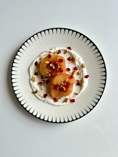 Top view of a peaches and cream dessert with nuts and pomegranate seeds on a stylish plate.