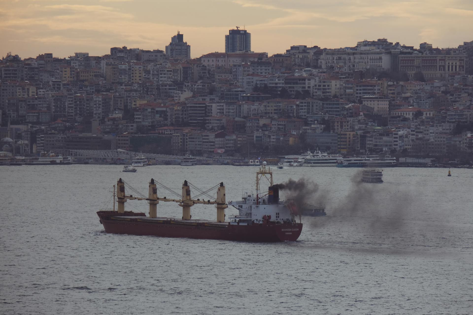 Industrial cargo ship sailing through the Bosporus with Istanbul's cityscape in the background at twilight.
