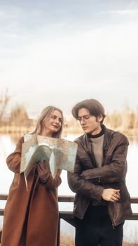 A young couple looks at a map outdoors near a serene lake, planning their adventure.