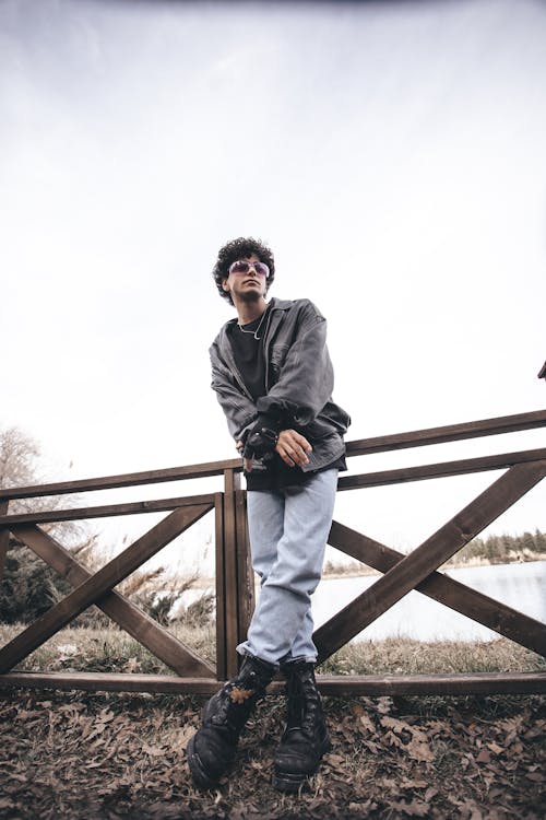 A man in jeans and jacket standing on a wooden fence