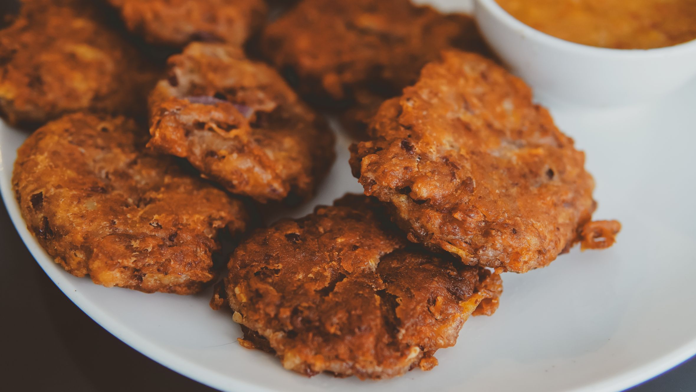 Delicious deep-fried fritters served with a tangy dip on a plate.