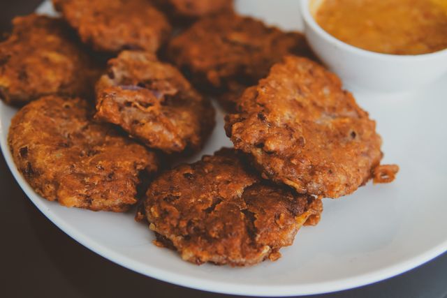 Delicious deep-fried fritters served with a tangy dip on a plate.