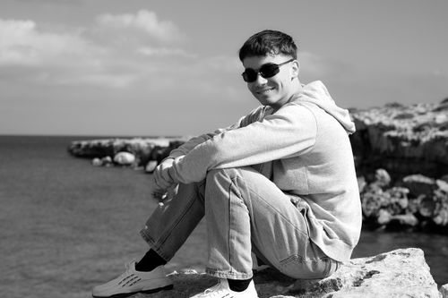 Free Black and white portrait of a young man sitting on rocks by the sea in Ayia Napa, Cyprus. Stock Photo