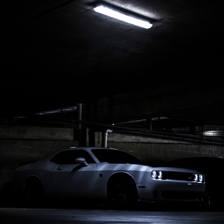 Free White Dodge Challenger Hellcat with headlights on, parked in a dimly lit parking garage in San Antonio. Stock Photo