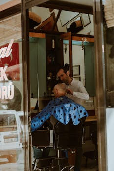 A barber gives an elderly man a haircut inside a cozy barbershop with a mirror view.