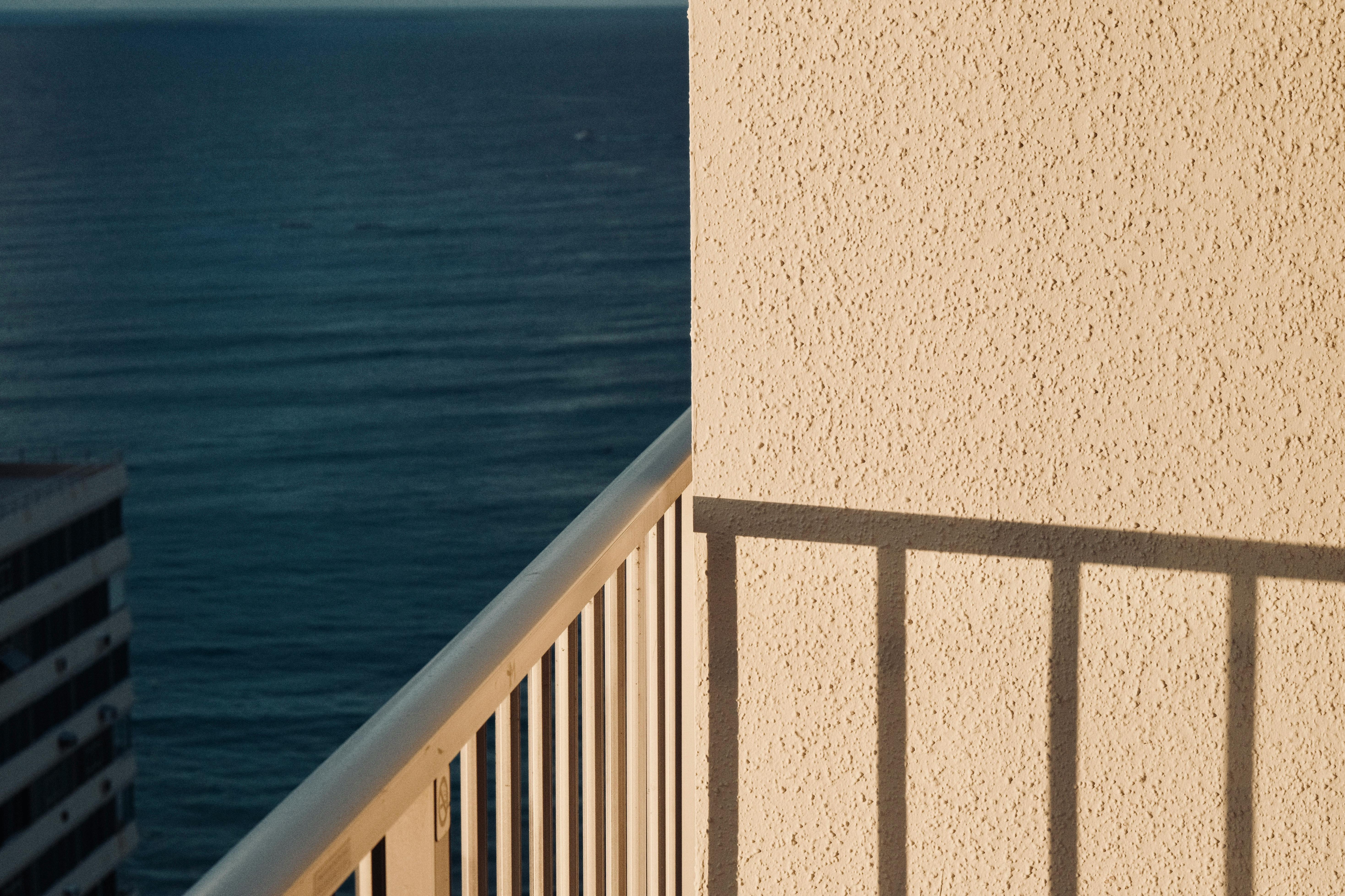 Sunlit balcony with ocean view in Honolulu, showcasing seaside tranquility and architectural shadows.