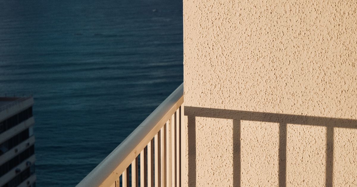 Varanda ensolarada com vista para o oceano em Honolulu, exibindo a tranquilidade à beira-mar e sombras arquitetônicas.