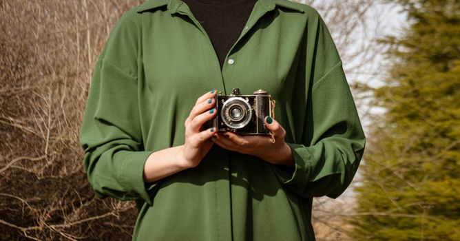 A woman in green shirt holds a vintage camera outdoors, capturing nostalgia.