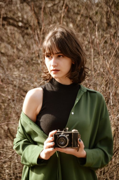 Free Caucasian woman with a vintage camera outdoors, modeling amidst rural natural landscape. Stock Photo