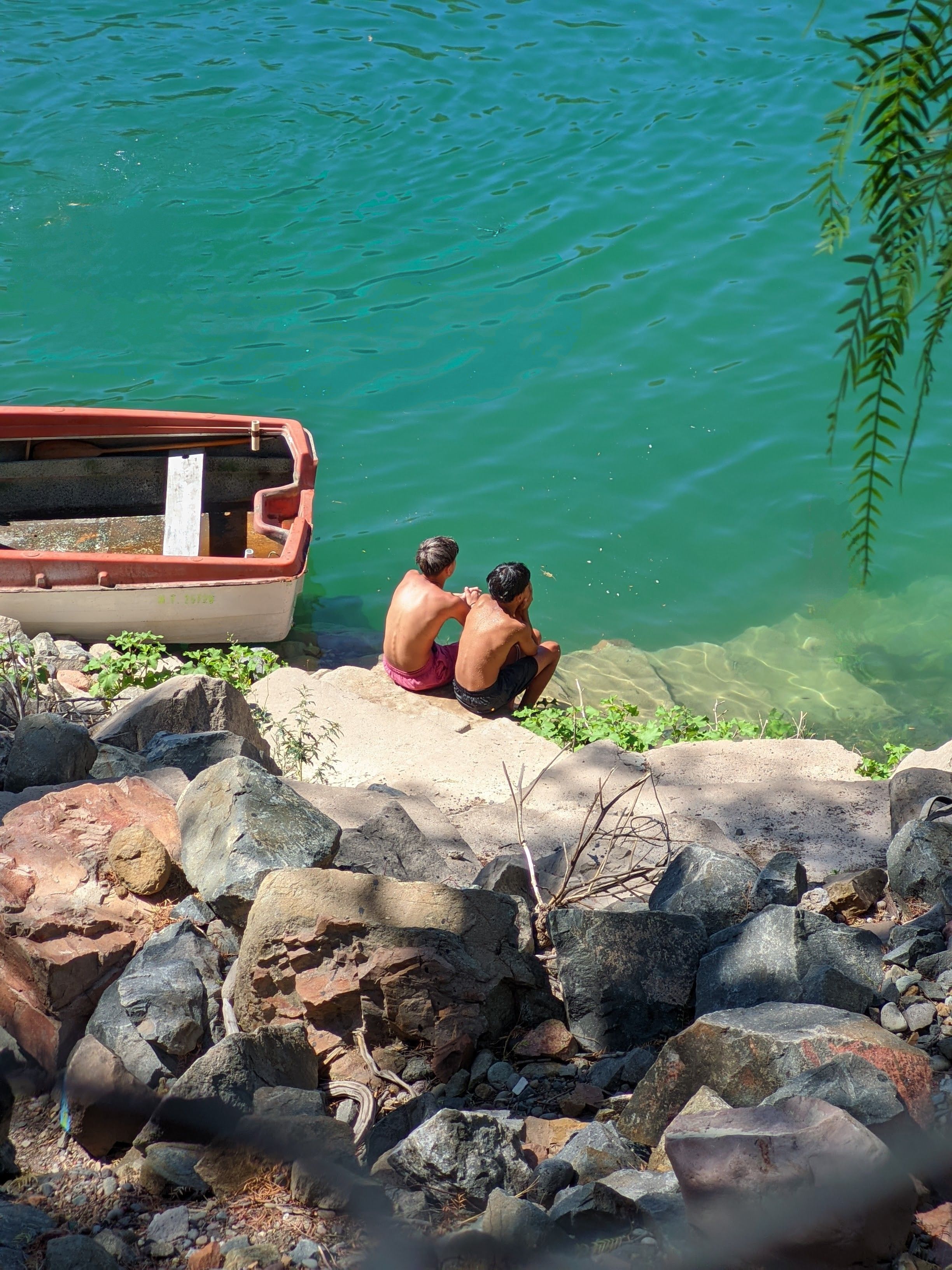 Two boys on a lakeshore with a boat in San Rafael, Argentina enjoying a summer day.