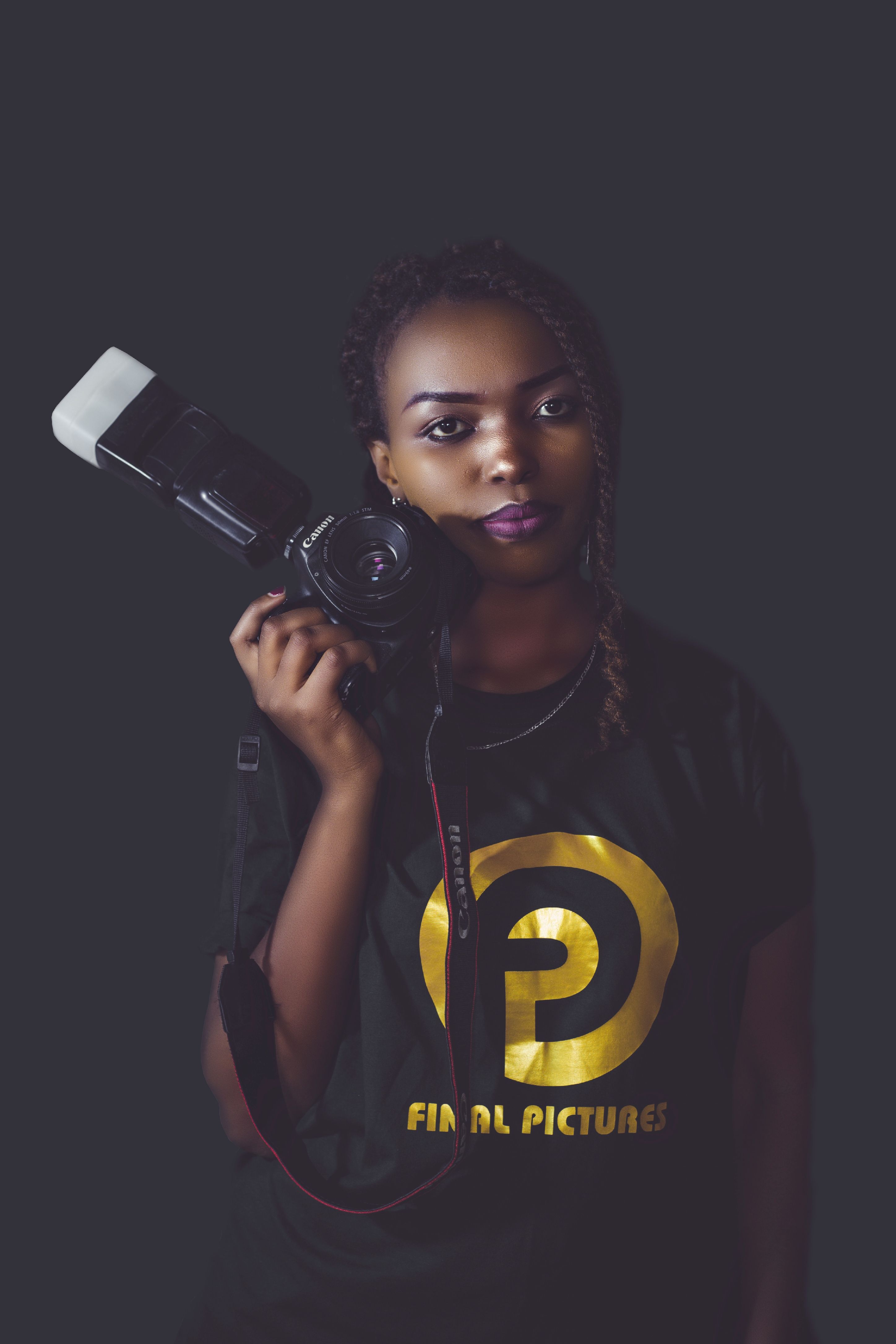 Portrait of a young black female photographer posing with a camera in a studio setting.