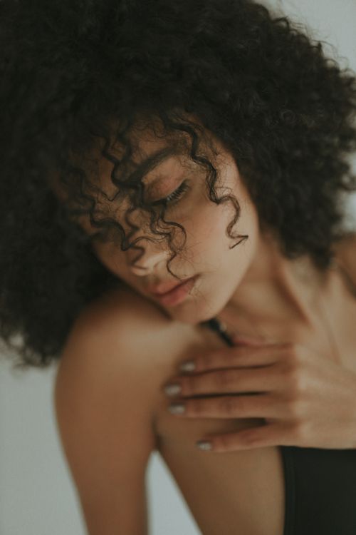 Free Close-up portrait of a young woman gently touching her shoulder with an introspective expression. Stock Photo