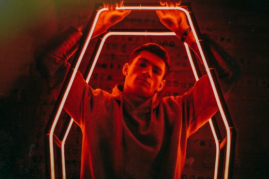 Man in hoodie posing with neon illumination adding dramatic effect.