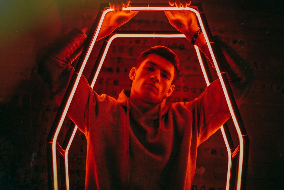 Man in hoodie posing with neon illumination adding dramatic effect.