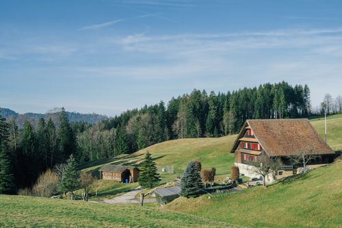 Free Charming rural scene with a farmhouse set against lush green hills and forests. Stock Photo