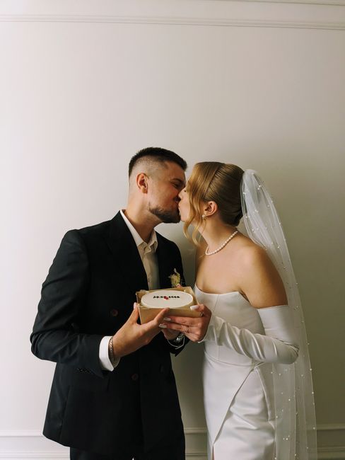 A newlywed couple shares a romantic kiss, holding a cake on their wedding day.