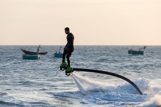 A man flyboards above the ocean, showcasing dynamic watersport adventure at sunset.