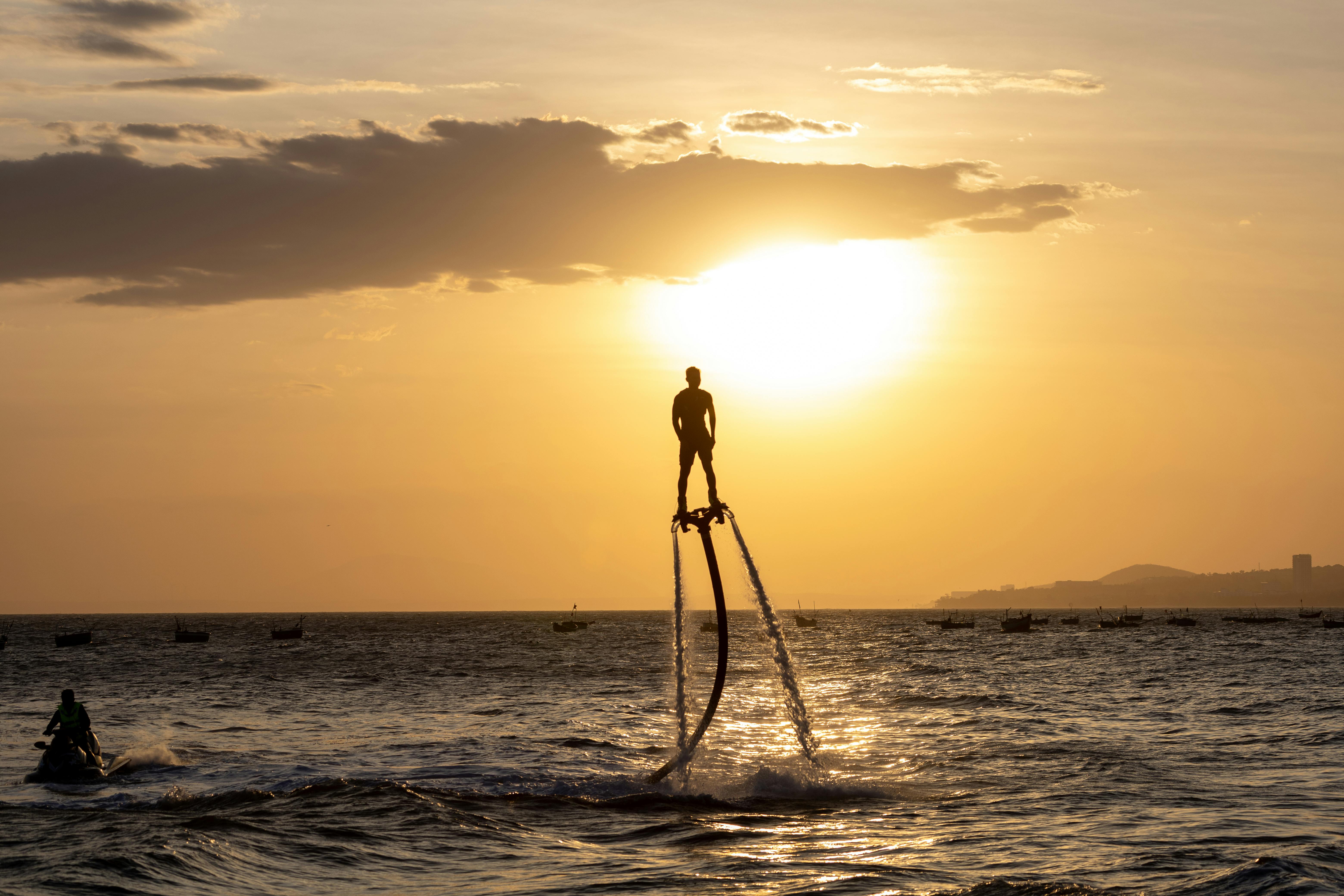 Silhouette of a man flyboarding at sunset over the sea, showcasing leisure and adventure.