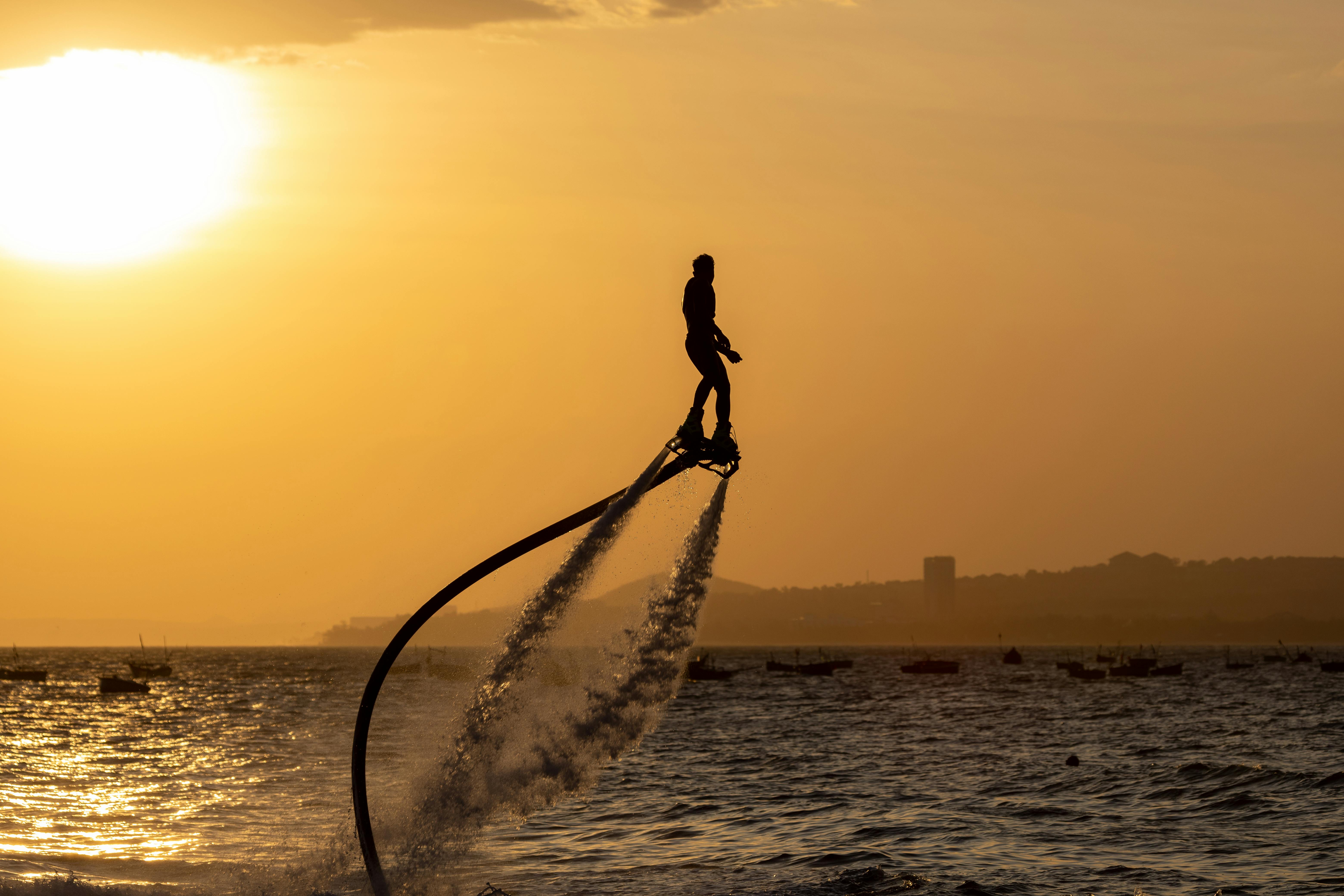 Dramatic silhouette of a man flyboarding against a golden sunset over the sea.