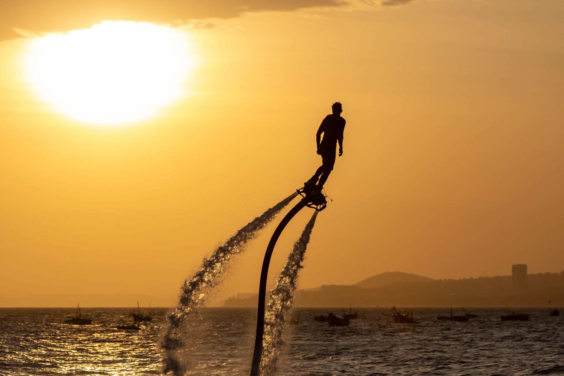 Silhouette of a man flyboarding against a stunning sunset over the sea.