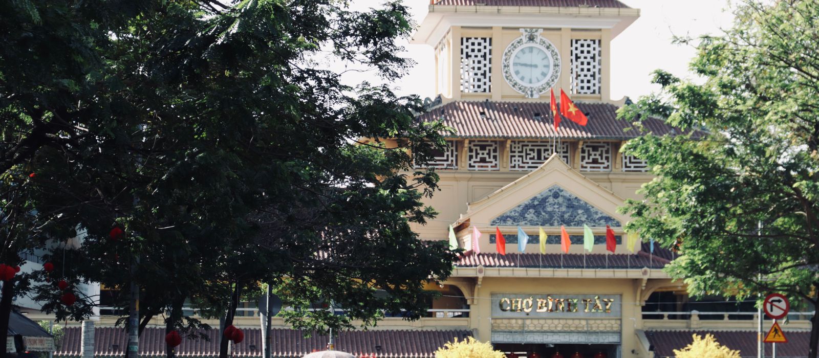 Scenic view of the iconic Binh Tay Market entrance with surrounding trees and vibrant flags in Ho Chi Minh City, Vietnam. — flights from Vientiane to Ho Chi Minh City